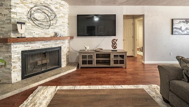 Uma sala de estar com lareira de pedra, uma TV de tela plana montada acima e um móvel de entretenimento cinza com objetos decorativos.