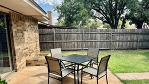 A patio with a table and chairs, a brick wall, a wooden fence, and a grassy yard.