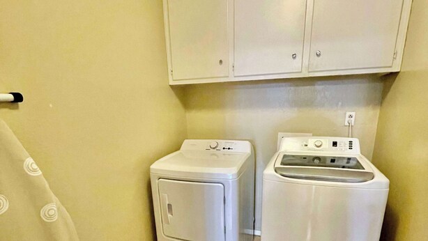 A laundry room with two white washing machines and a cabinet above them.