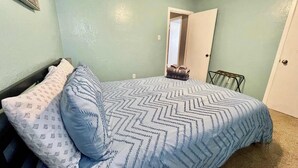 A bedroom with a bed, pillows, a door, and a towel rack.