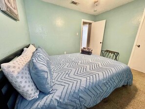 A bedroom with a bed, pillows, a door, and a towel rack.