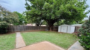 A backyard with a grassy area, a concrete patio, a wooden fence, a tree, and a shed.