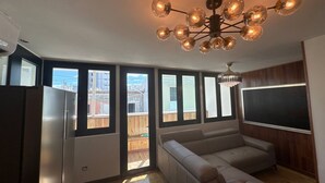 Un salon moderne avec un grand canapé, un lustre et une grande fenêtre donnant sur une terrasse.