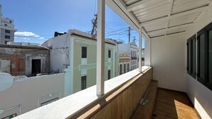 Un balcon donnant sur des immeubles, avec un plancher en bois et un plafond blanc.