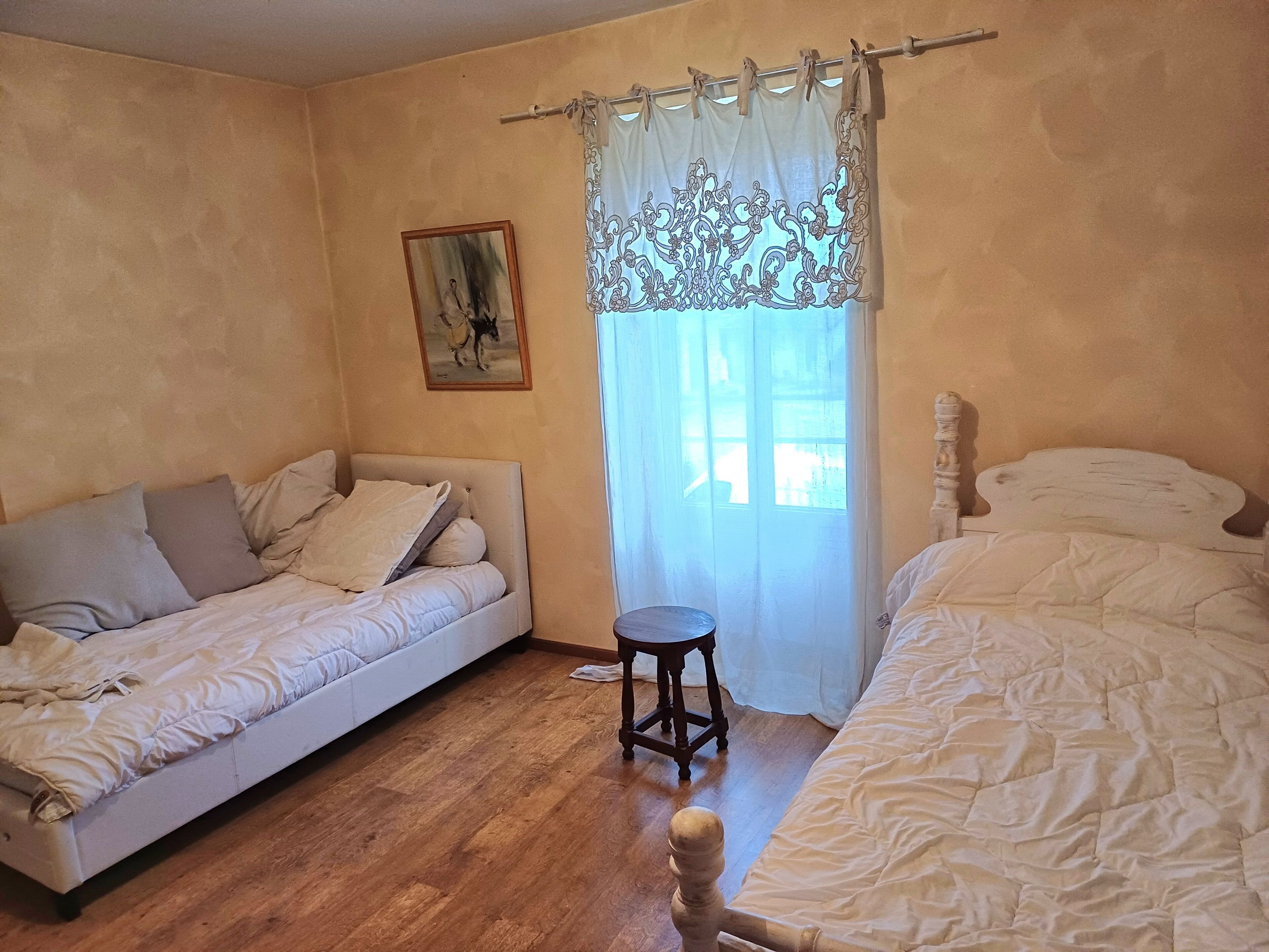 A bedroom with two beds, a wooden floor, a small stool, and a painting on the wall.
