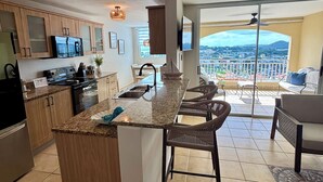 Cocina moderna con isla central, comedor con sillas de mimbre y balcón con vista a la ciudad.