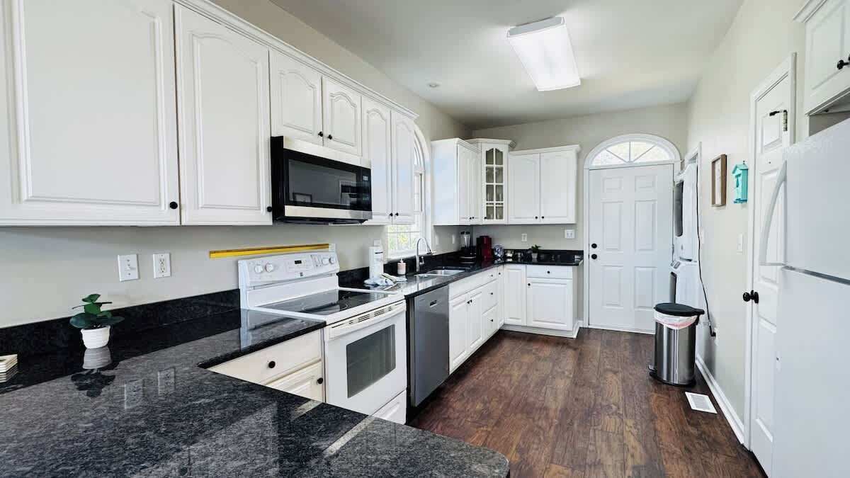 A kitchen with white cabinetry, a black countertop, a microwave, an oven, and a dishwasher.