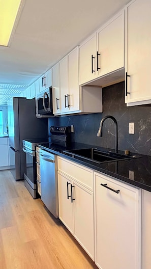 A modern kitchen with white cabinets, black countertops, and stainless steel appliances. - Ocean Villas apartment, view the ocean and relax (Myrtle Beach)