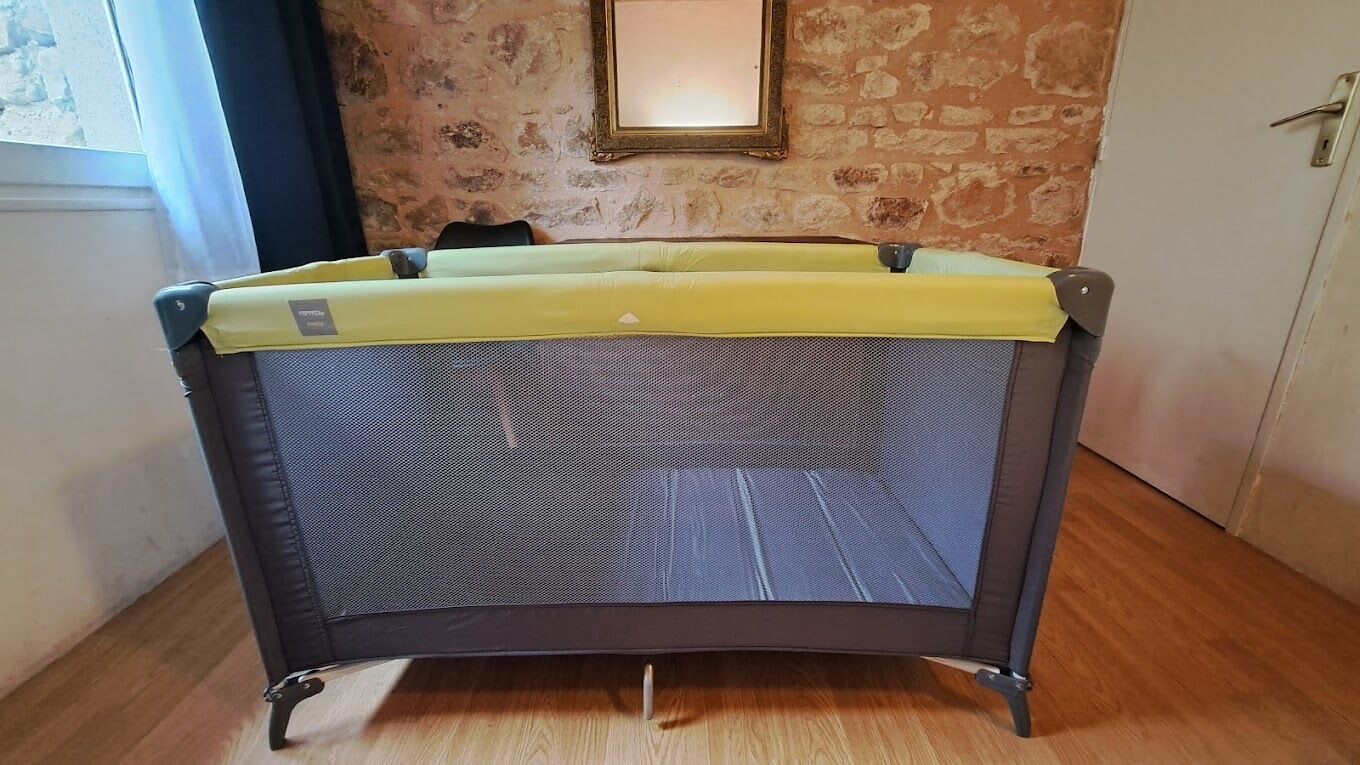 A room with a grey foldable bed, a wooden floor, a stone wall, and a door with a handle.