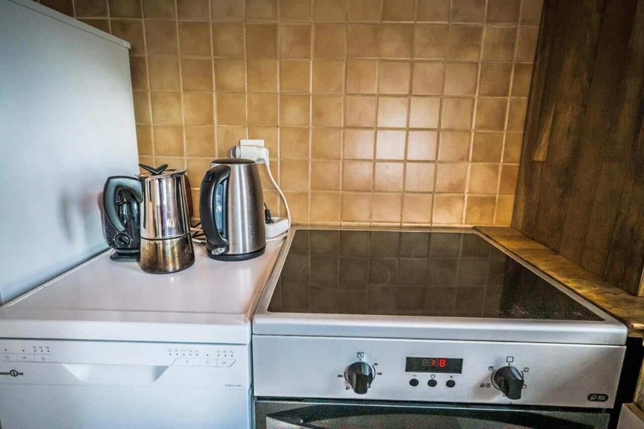 Une cuisine équipée d’une cuisinière, d’une bouilloire et d’une machine à café, le tout posé sur le plan de travail.