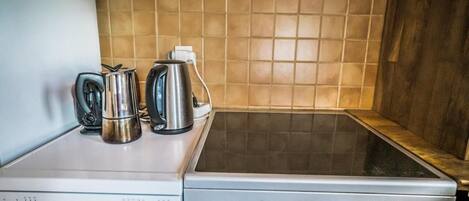 Une cuisine équipée d’une cuisinière, d’une bouilloire et d’une machine à café, le tout posé sur le plan de travail.