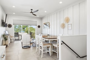 A modern interior with a dining area, white walls, ceiling fan, and a view to the outdoors. - Gulfside Sunset - 2309B   “Anna Maria Island” (Bradenton Beach)