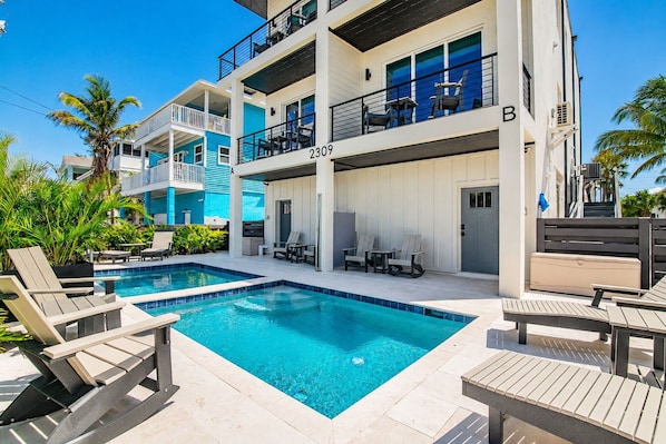 A multi-story hotel with a swimming pool, outdoor seating, and a view of the surrounding area.