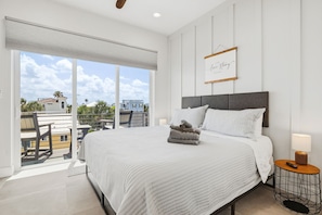 A bedroom with a large bed, a bedside table, a view of the outdoors, and a framed quote on the wall. - Gulfside Sunset - 2309B   “Anna Maria Island” (Bradenton Beach)