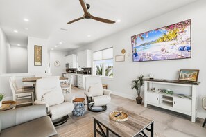 A modern living room with a ceiling fan, a large painting, and a dining area with a table and chairs. - Gulfside Sunset - 2309B   “Anna Maria Island” (Bradenton Beach)