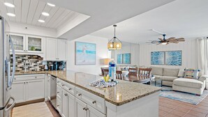 Una cocina moderna con encimeras de granito, armarios blancos y un comedor con sofá blanco y una mesa de centro.