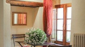 A cozy dining area with a table, chairs, a flower centerpiece, and a window with curtains. - PienzaLettings Suites (Pienza)