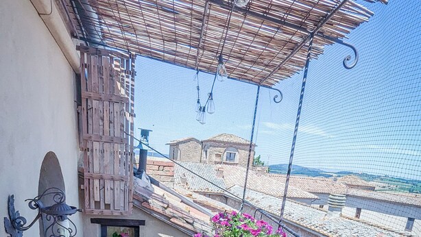 A balcony with a metal railing, a small table with a chair, potted plants, and a view of the sea. - PienzaLettings Suites (Pienza)