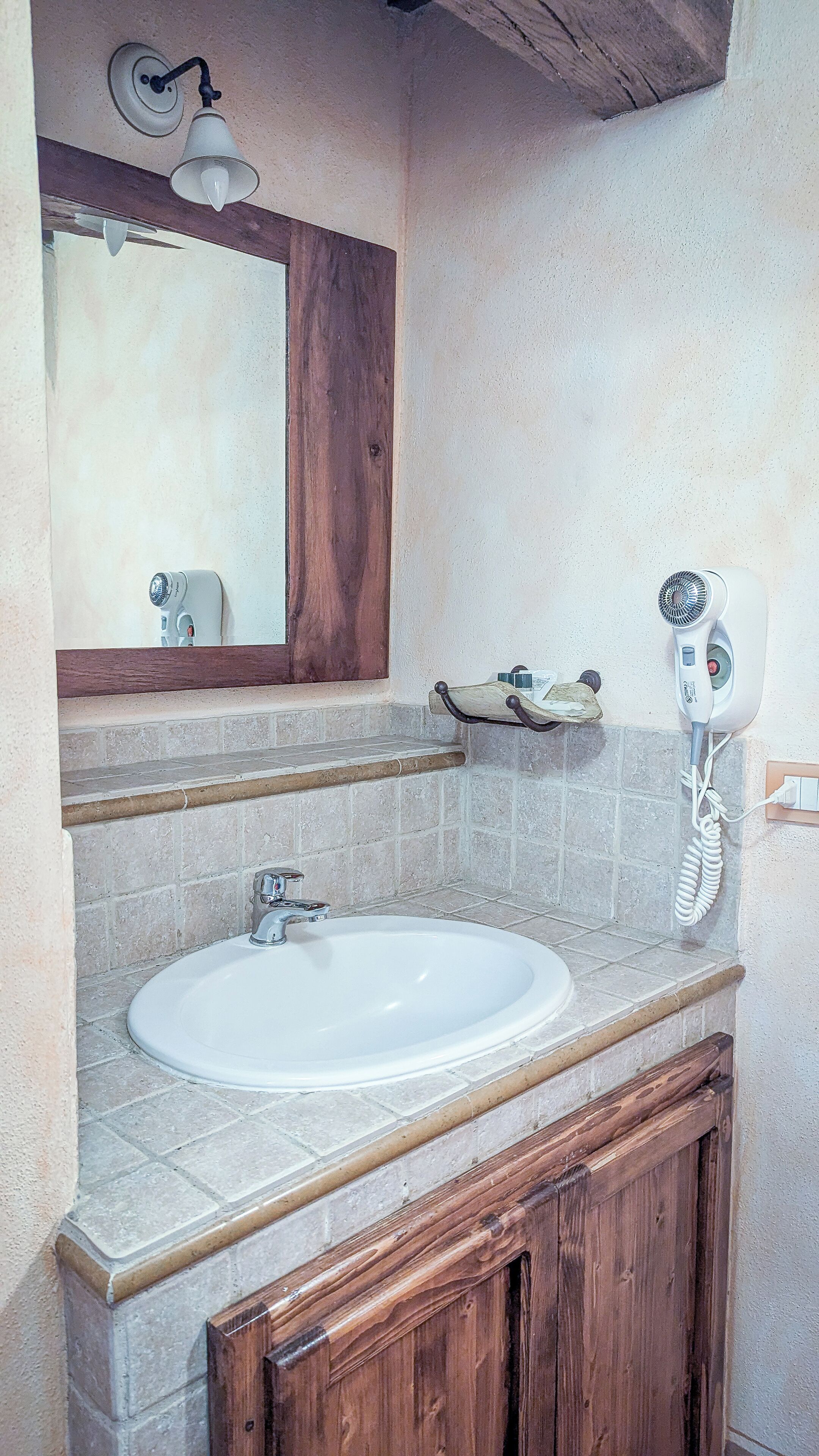 Casa de banho com uma pia branca, um armário de madeira, um espelho e um secador de cabelo na parede.
