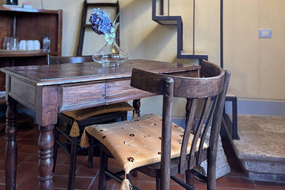 A wooden dining table with chairs, a vase with flowers, and a staircase in the background.