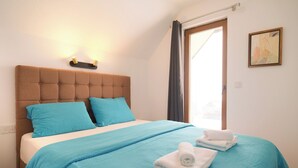 Un lit bien fait, avec une couvre-lit bleue et des oreillers, une tête de lit capitonnée et une fenêtre avec des rideaux.