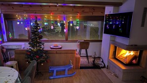 Un salon chaleureux avec une cheminée, un sapin de Noël et un téléviseur fixé au mur.