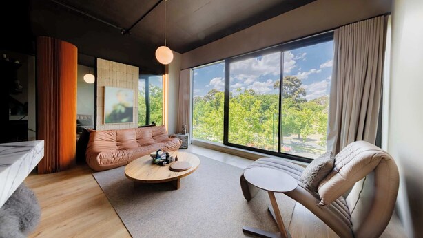 Quarto moderno com sofá, poltrona, mesa de centro e uma grande janela com vista para árvores.