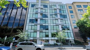 Um edifício de vários andares com fachada de vidro, uma placa de estacionamento e vista para a rua.