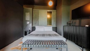 Quarto moderno com cama, luminária de cabeceira e um banquinho.