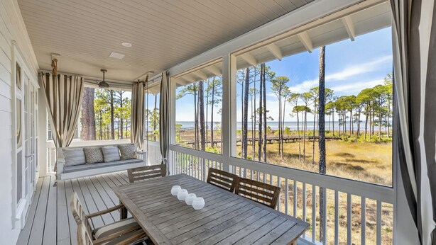 A covered outdoor seating area with a wooden table and chairs, a bench with cushions, and a view of the beach and trees. - Elevated Vacation Living• Fairmont Inspiration by the Bay (Miramar Beach)