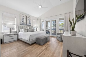 A modern bedroom with a large bed, a nightstand, a desk, and a balcony with curtains.