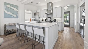 A modern kitchen with a large island, white cabinetry, stainless steel appliances, and a view to the outdoors. - Elevated Vacation Living• Fairmont Inspiration by the Bay (Miramar Beach)