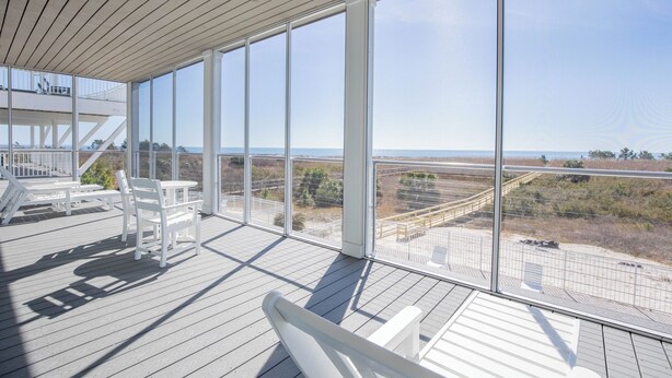 A spacious balcony with white furniture and large windows offering a view of the beach and ocean. - Gulf front, elevator, private pool, outdoor dining, beach gear! (PORT SAINT JOE)