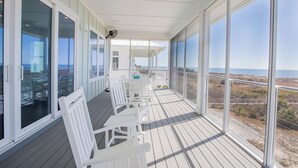 A covered outdoor deck with white chairs and tables, large windows offering a view of the beach and ocean. - Gulf front, elevator, private pool, outdoor dining, beach gear! (PORT SAINT JOE)