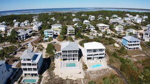 A coastal residential area with multiple two-story houses, a large swimming pool, and a beach in the background. - Gulf front, elevator, private pool, outdoor dining, beach gear! (PORT SAINT JOE)