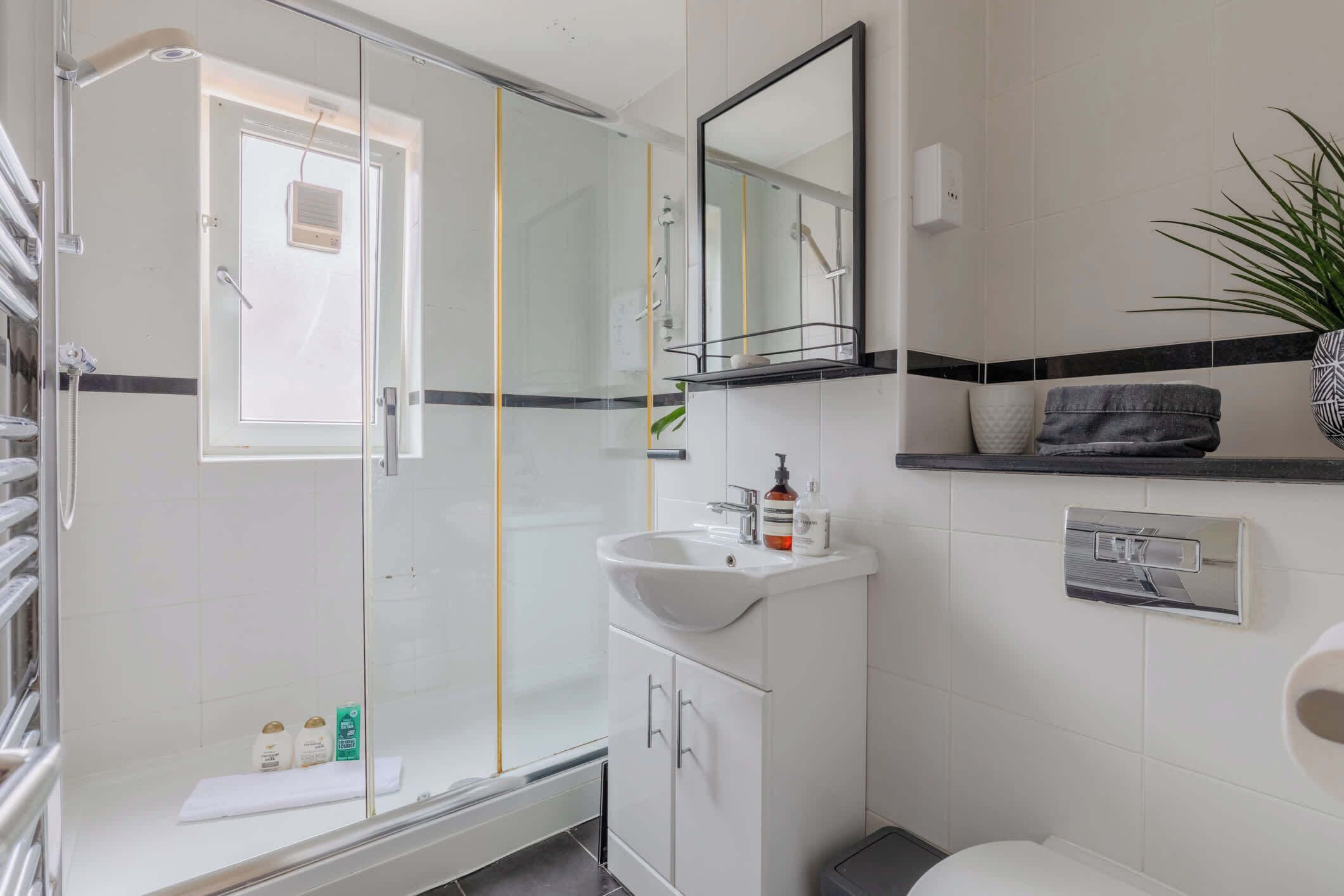 Une salle de bain moderne avec une douche à parois de verre, un lavabo blanc avec un miroir au-dessus et des toilettes.