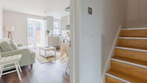 A modern living room with a sofa, a coffee table, and a chair. There is a staircase leading to another level. - Cosy 4BD Flat in Stockwell with Private Patio (Greater London)