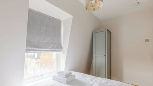 A bedroom with a bed, a window with a view, a wardrobe, and a ceiling light fixture. - Cosy 4BD Flat in Stockwell with Private Patio (Greater London)
