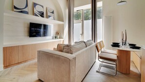 A modern living room with a sofa, a TV mounted on the wall, and a dining area with a table and chairs.