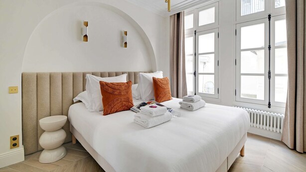 A hotel room with a large bed, a bedside table, a radiator, and a window with curtains.