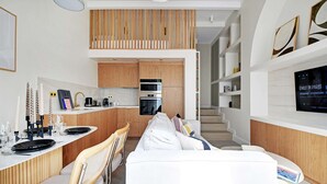 A modern kitchen with wooden cabinets, a built-in oven, and a dining area with a white sofa and chairs.