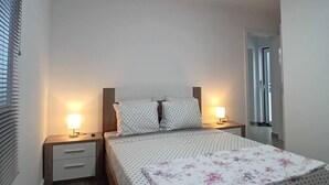 Un dormitorio con una cama, dos mesitas de noche con lámparas, un cabecero de madera y una lámpara en el techo.