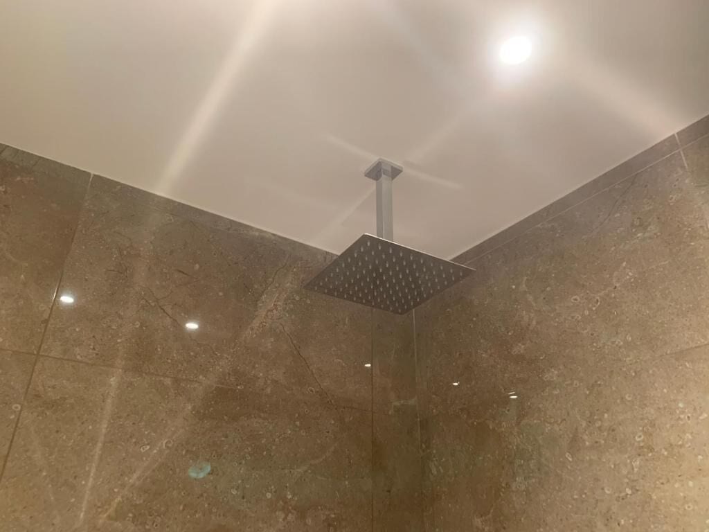 Une douche dotée d’un plafond carré perforé et entourée de murs en pierre polie.