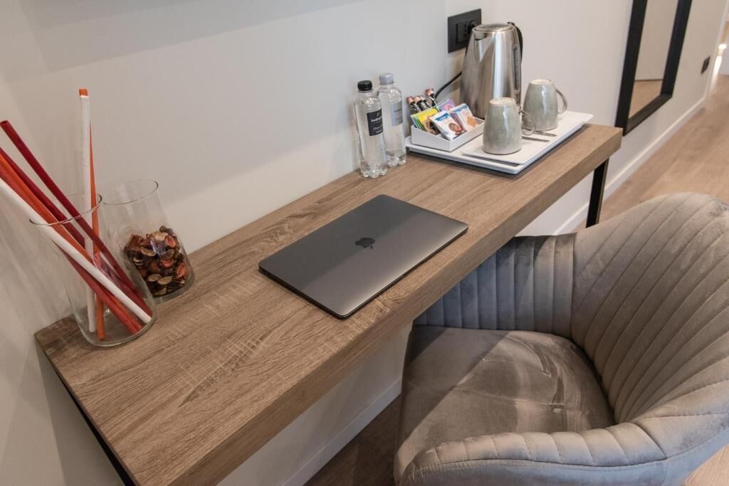 A wooden desk with a laptop, a coffee maker, and a glass with pencils.