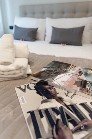 Una cama bien hecha con un cabecero gris, una pila de toallas blancas y una revista sobre la cama.