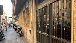A narrow street with parked motorcycles and cars, a building with a large metal gate, and a sidewalk with a tactile paving strip. - XXIV Domus Luxury Suites (Rome)
