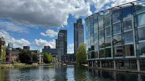 A modern building with large glass windows, a river in the foreground, and several other buildings in the background. - Private En-Suite Room | Walk to Angel Station | Near Shoreditch (London)