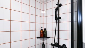 A shower with a handheld showerhead, a wall-mounted shelf with toiletries, and a tiled wall with a grid pattern. - Large Private En-Suite Room | Walk to Angel Station (London)
