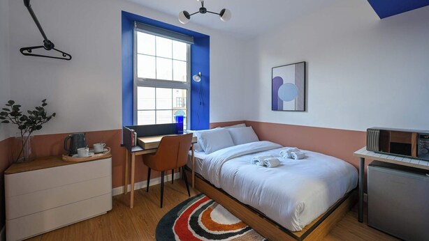 A bedroom with a bed, desk, chair, and a small kitchenette. - Large Private En-Suite Room | Walk to Angel Station (London)