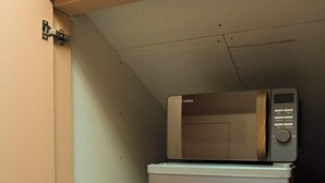A compact refrigerator with a microwave on top, placed inside a cabinet with a hinged door. - Modern Loft En-Suite Room in Angel | Walk to Tube (London)